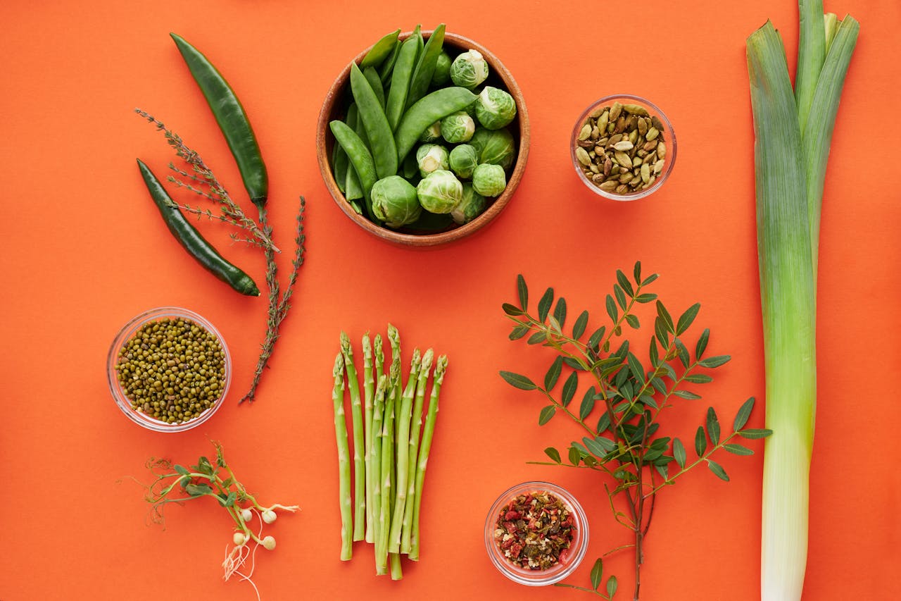 Services Top view of assorted green vegetables and herbs on a bold orange background, showcasing freshness.